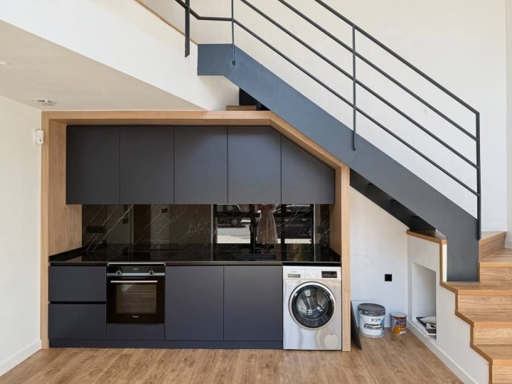 Cocina abierta en negro junto a la escalera de madera