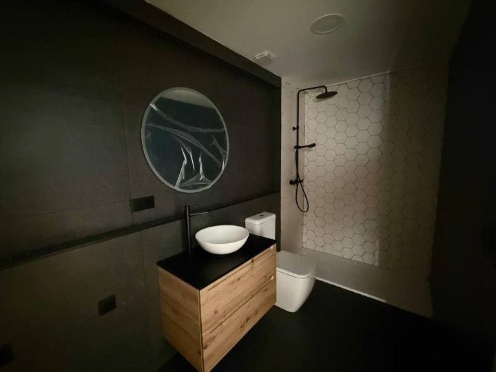 Baño con mueble de madera y espejo redondo